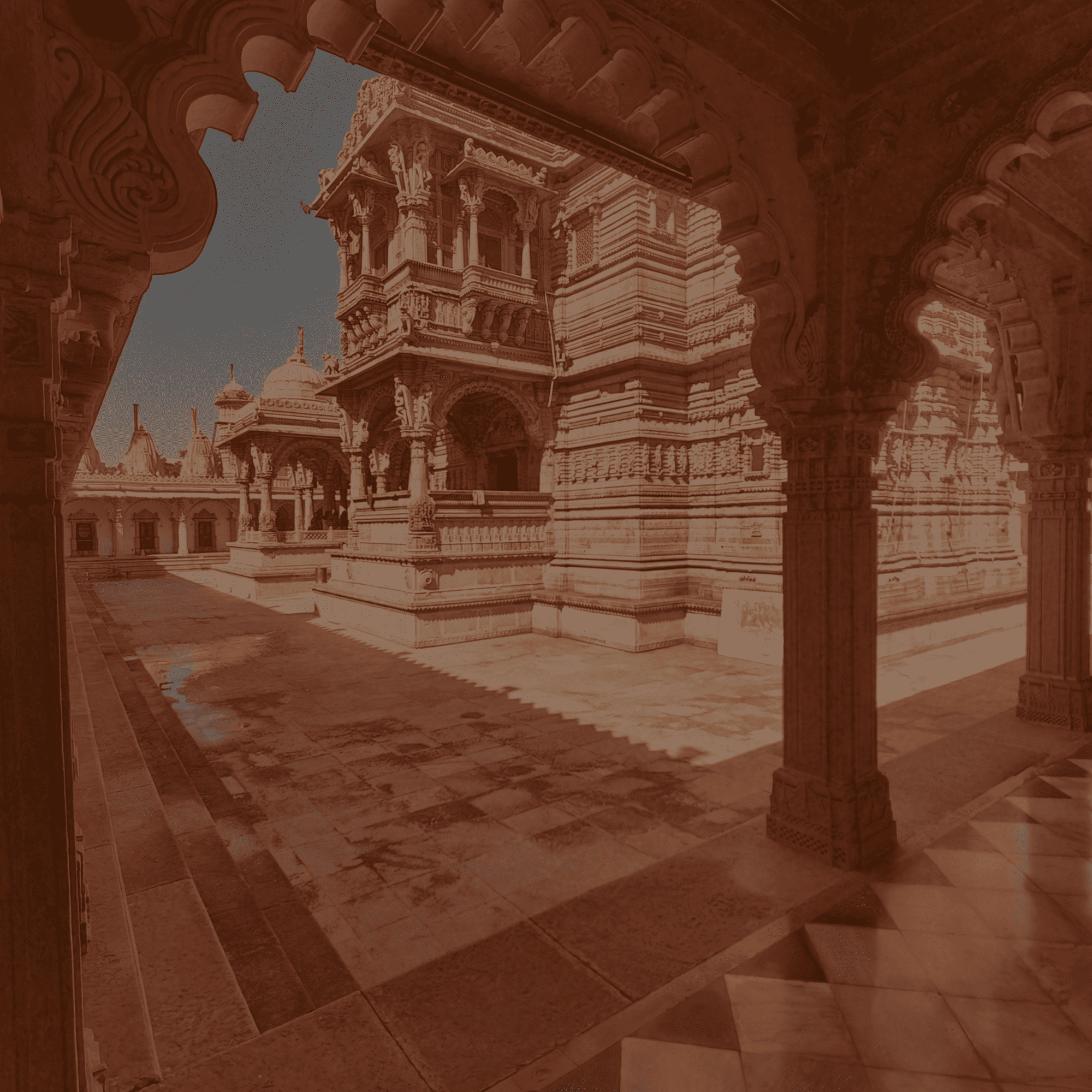 A view from within an ornate stone corridor looking out onto a grand, intricately carved temple courtyard under a clear blue sky.