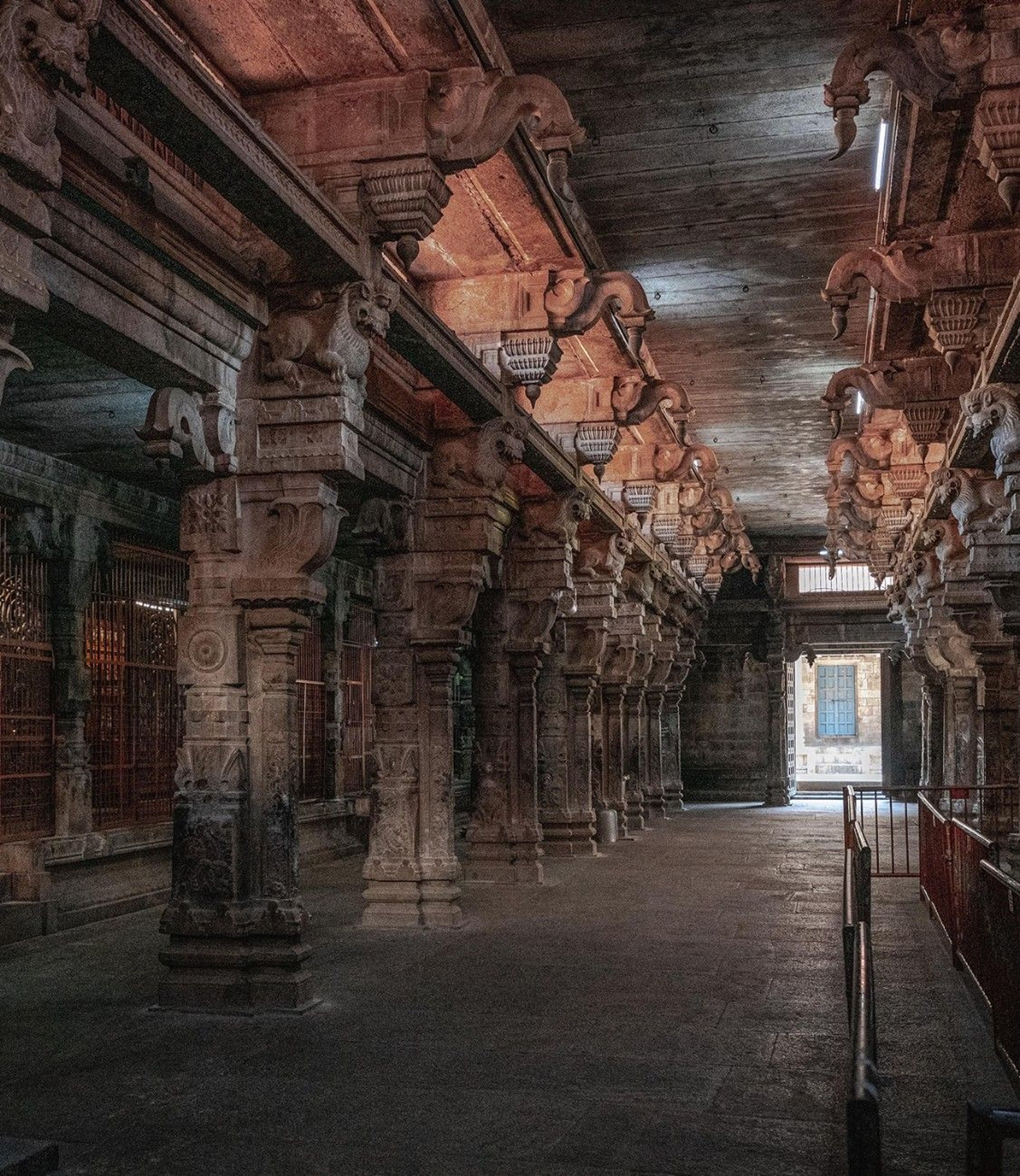 A narrow stone corridor inside a historic temple hall, with carved pillars, ornate ceiling details, and warm brown and gray stone tones.